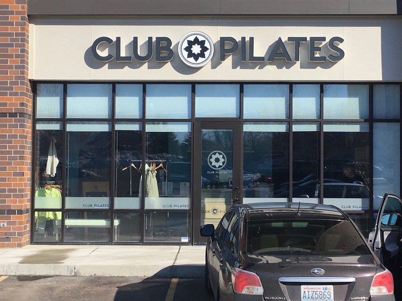 Club Pilates storefront with sign, logo, and glass windows. A car is parked out front.