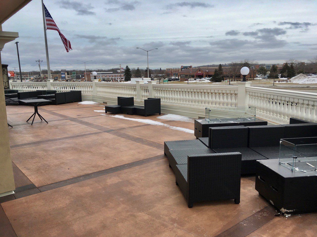Outdoor patio with black furniture, white balustrade, American flag. Overcast sky, some snow on ground.