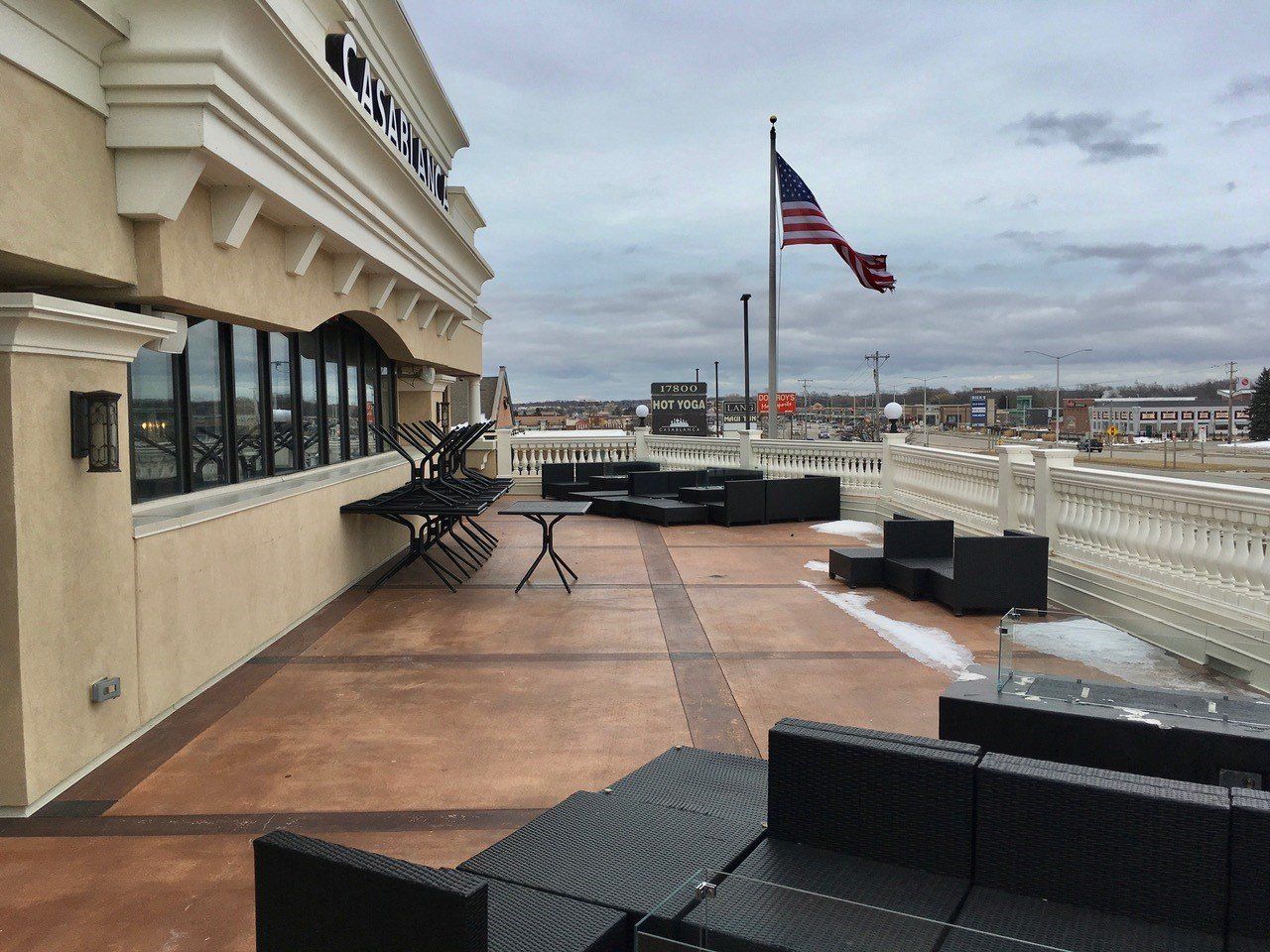 Rooftop patio with seating, American flag, and overcast sky. Building exterior with windows.