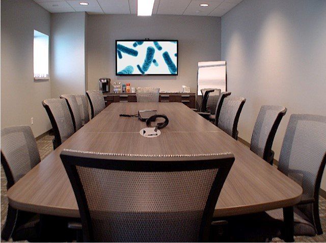 Conference room with long table, chairs, and a screen displaying blue shapes.