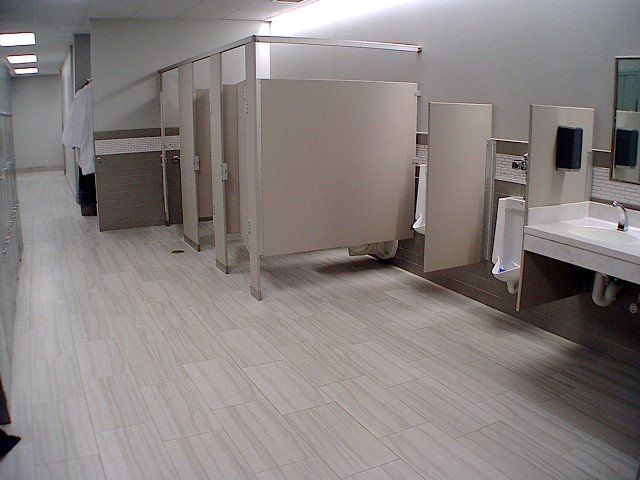 Public restroom with stalls, urinals, and sinks; light-colored tile floor.