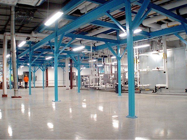Blue support beams in a large, empty industrial space with polished concrete floors and overhead lighting.