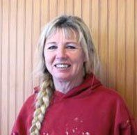 A woman in a red hoodie is smiling in front of a wooden wall. Marci