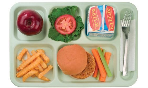 A divided school lunch tray with a burger, fries, carrot and celery sticks, a slice of tomato, lettuce, an apple, and milk.