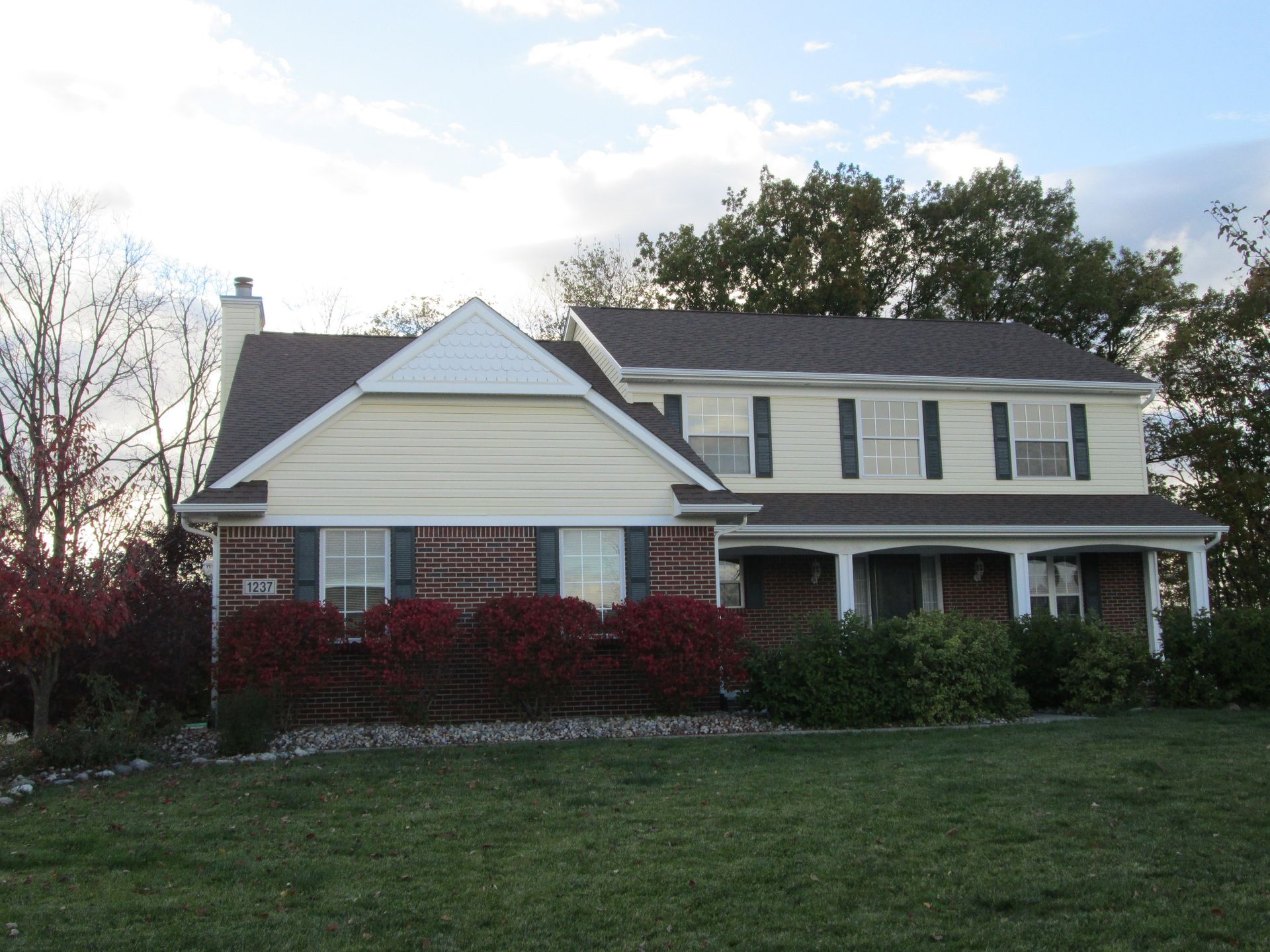 Suburban house with white siding, brick accents, and a front lawn under a cloudy sky