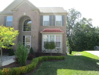 Brick townhouse with arched window, red awning, and green lawn in bright sunlight