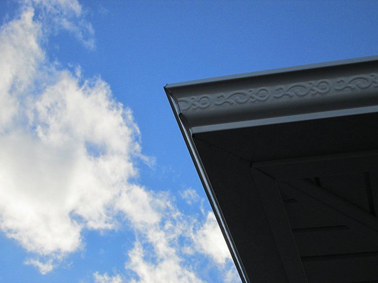 Blue sky with clouds beside the corner of a dark roof with decorative trim
