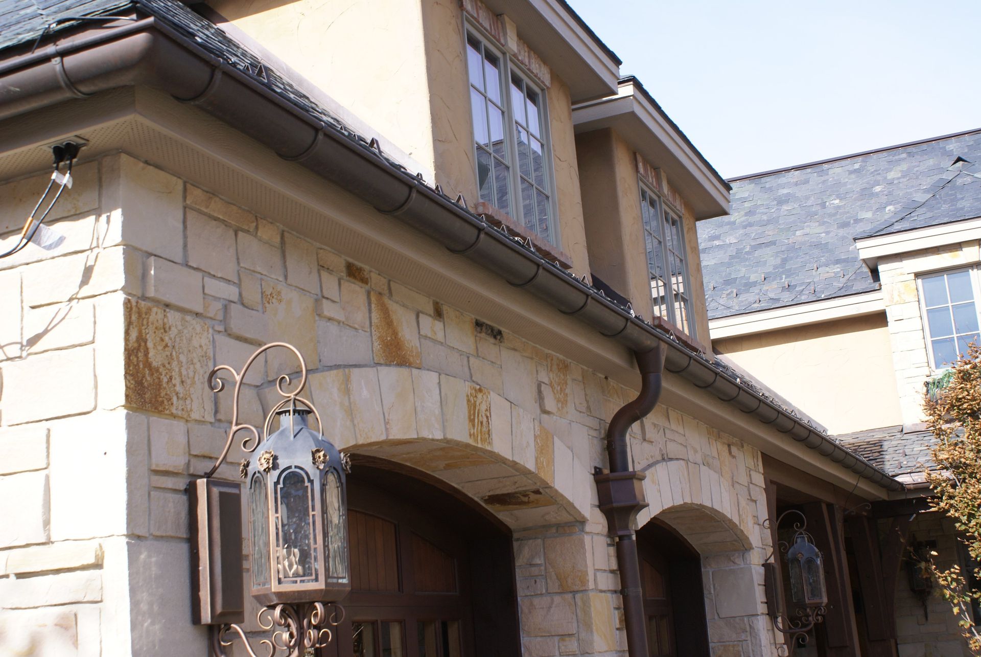 Stone building exterior with arched entryways, tan walls, and a lantern by the doorway