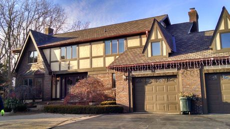 Suburban two-story brick house with tan siding, attached garage, and leafless trees in front