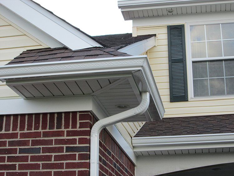 Gutter downspout on a house roofline above brick and beige siding