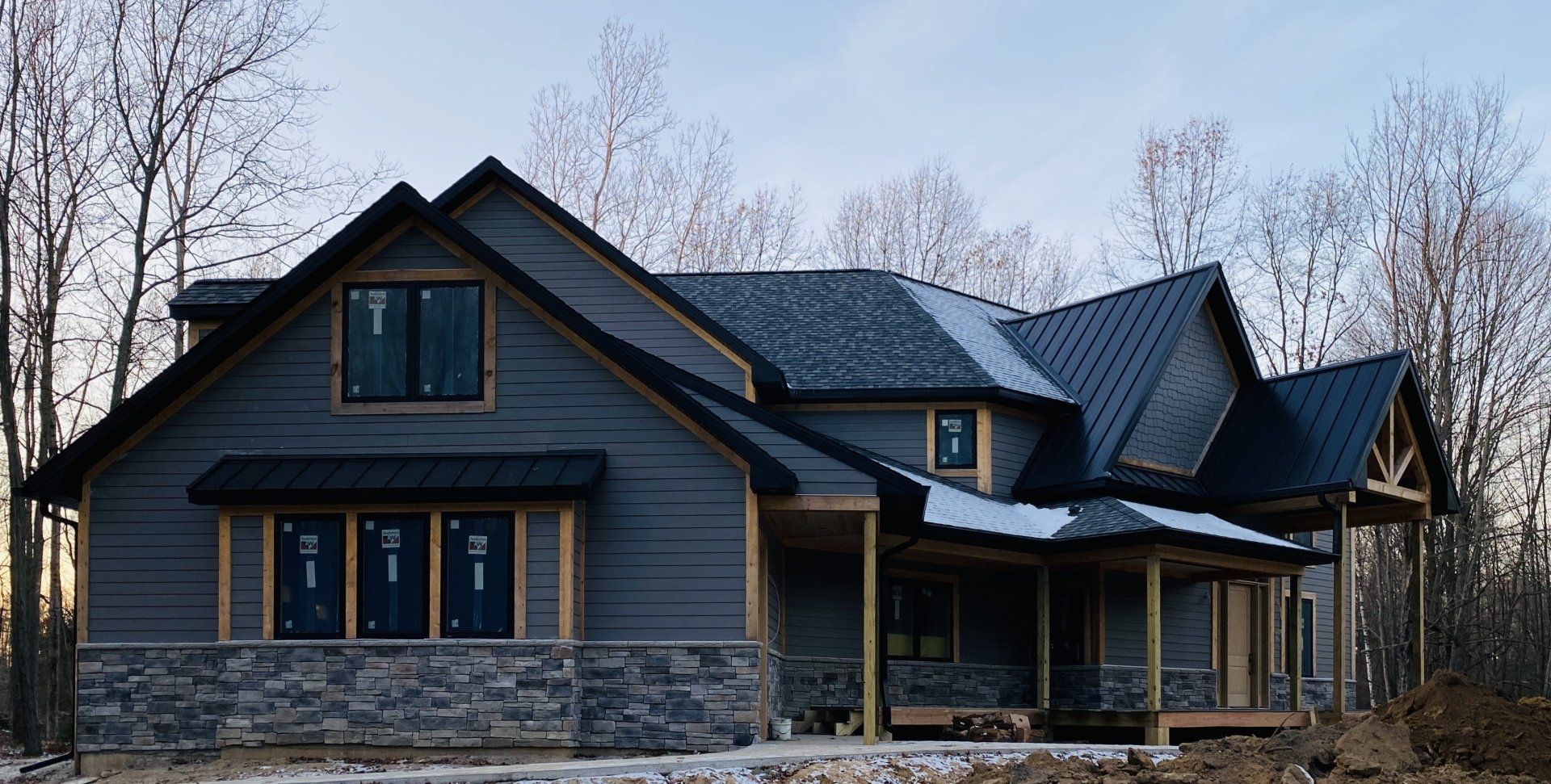 Dark-blue modern house with stone accents and a covered porch in a wooded setting