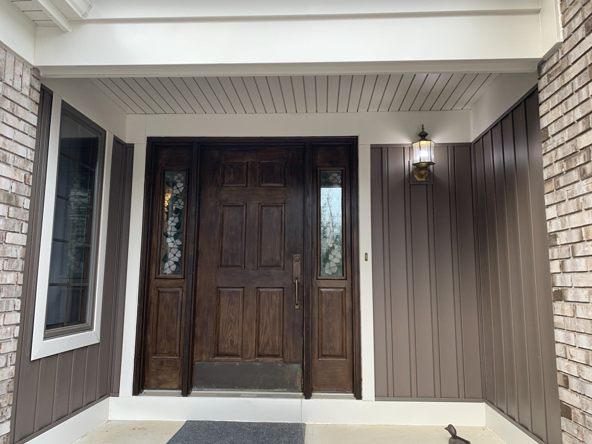 Front porch with dark wood double doors, white trim, brick columns, and a wall lantern