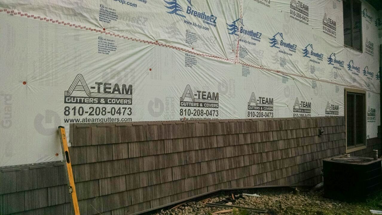 House under construction with wrapped exterior walls and shingled lower siding at the back.