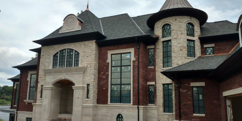 Large stone-and-brick mansion with arched entrance, tall windows, and dark shingled roofs under a cloudy sky