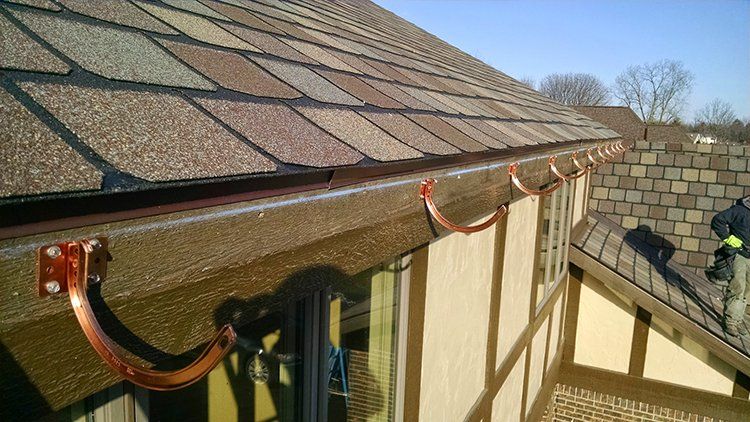 Roof edge with red holiday lights draped along the eaves beside a brick wall and blue sky