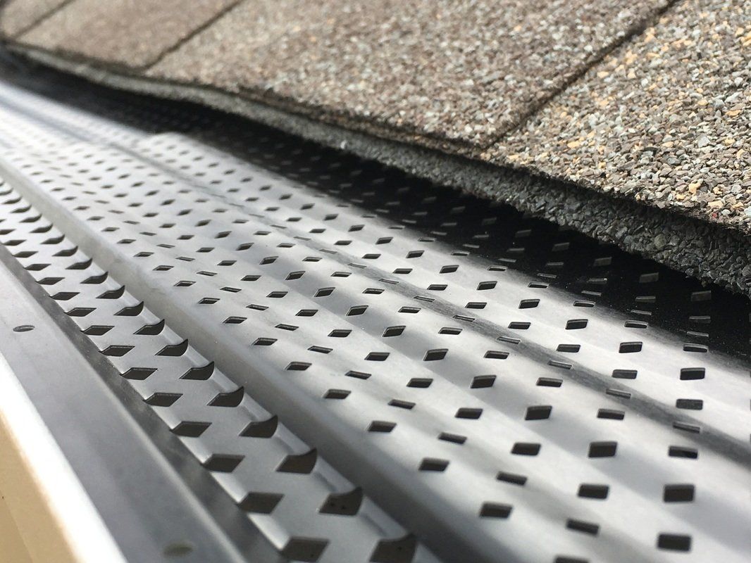 Close-up of a roof edge with metal gutter guard under gray shingles