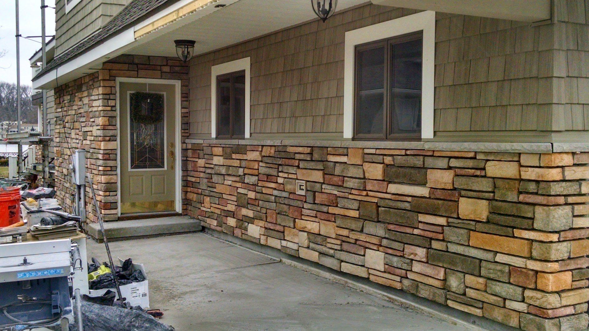 House exterior with tan siding, stone veneer, and a concrete walkway under construction