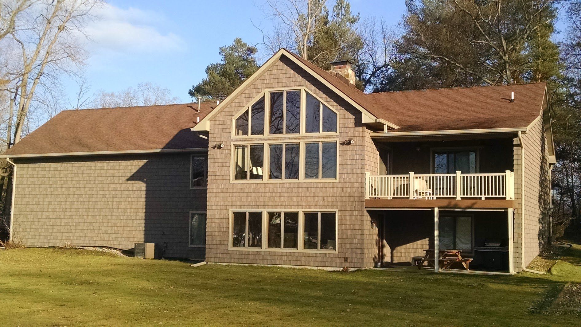 Large stone house with tall central windows, brown roof, and a covered porch on a grassy lawn.