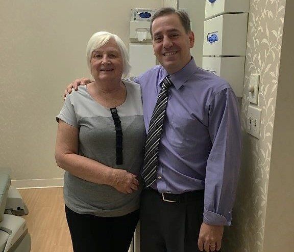 Two people standing together in a clinic hallway, smiling beside medical cabinets.