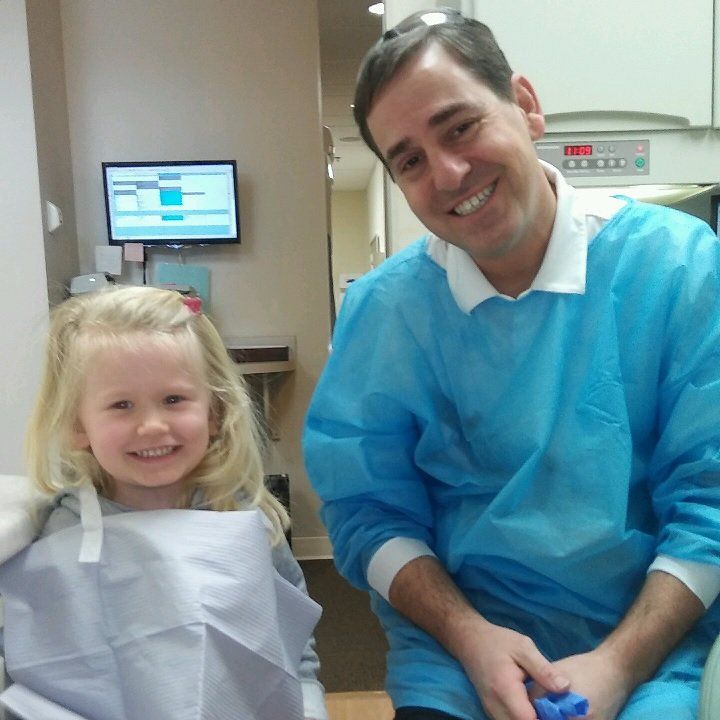 Smiling child and adult in blue dental gowns in a clinic room