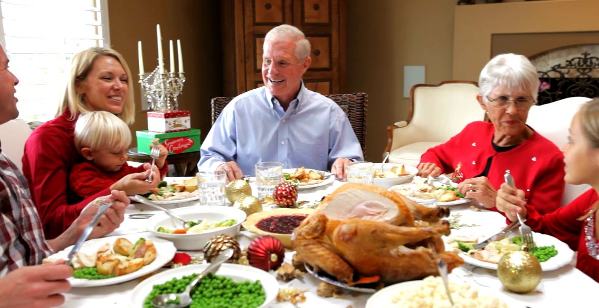 Family gathered around a table for a holiday meal, with a roast turkey and side dishes.