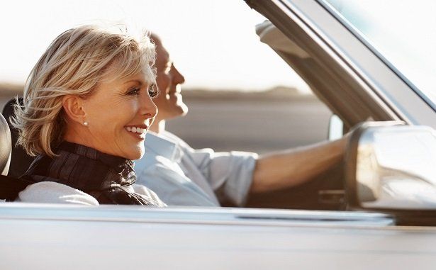 Two people smiling in a convertible car, driving with the top down in bright sunlight