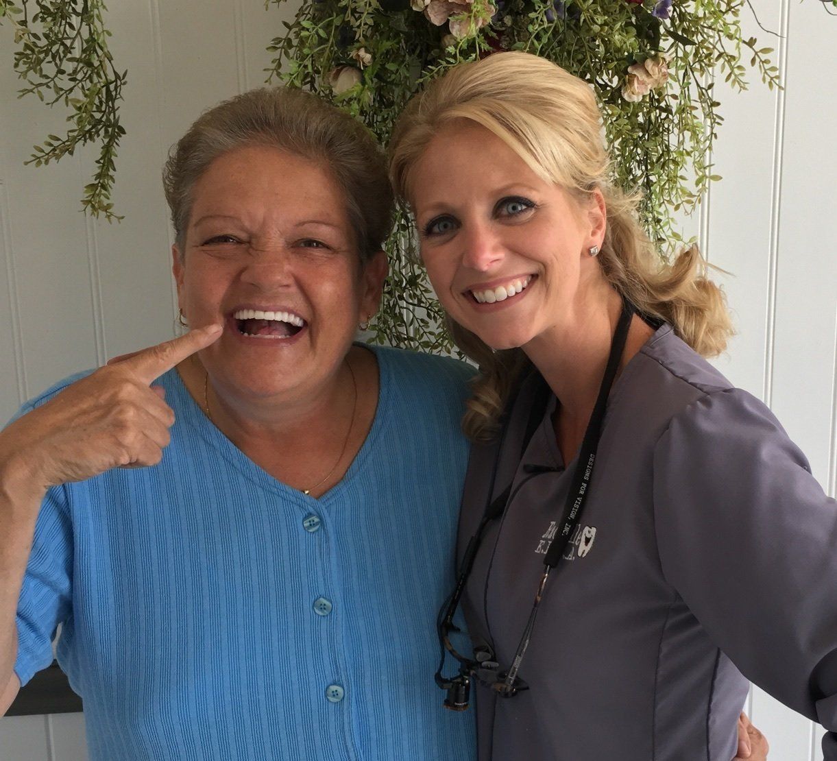 Two smiling women standing together, one in a blue sweater and one in a gray shirt with a stethoscope