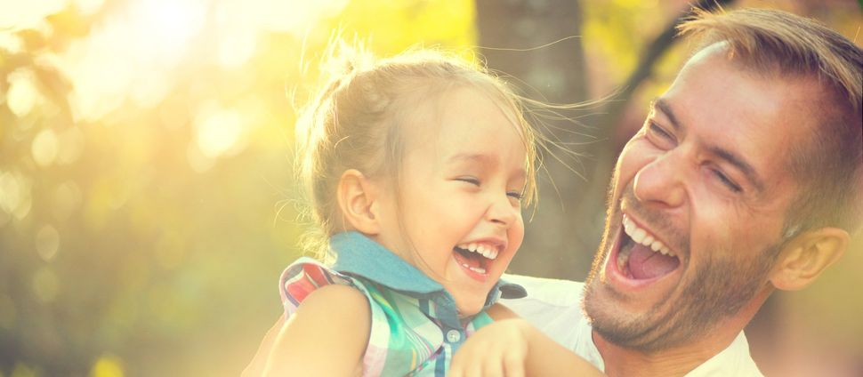 A man is holding a little girl in his arms and they are laughing.