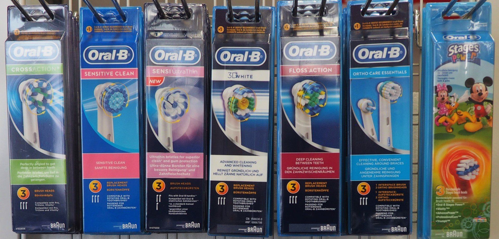 Una fila di confezioni di spazzolini Oral-B, con imballaggio blu e nero, su uno scaffale di un negozio.