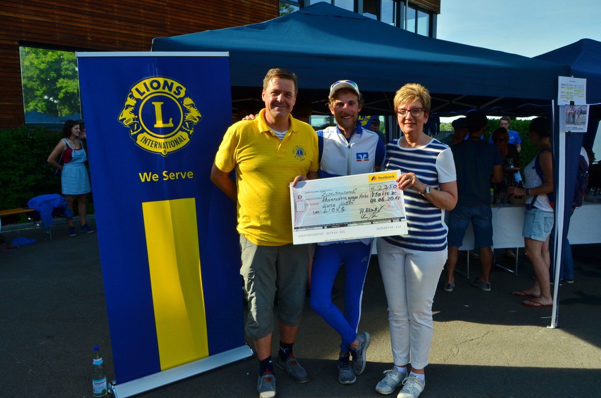 Drei Personen halten einen Scheck vor einem Lions Club Banner