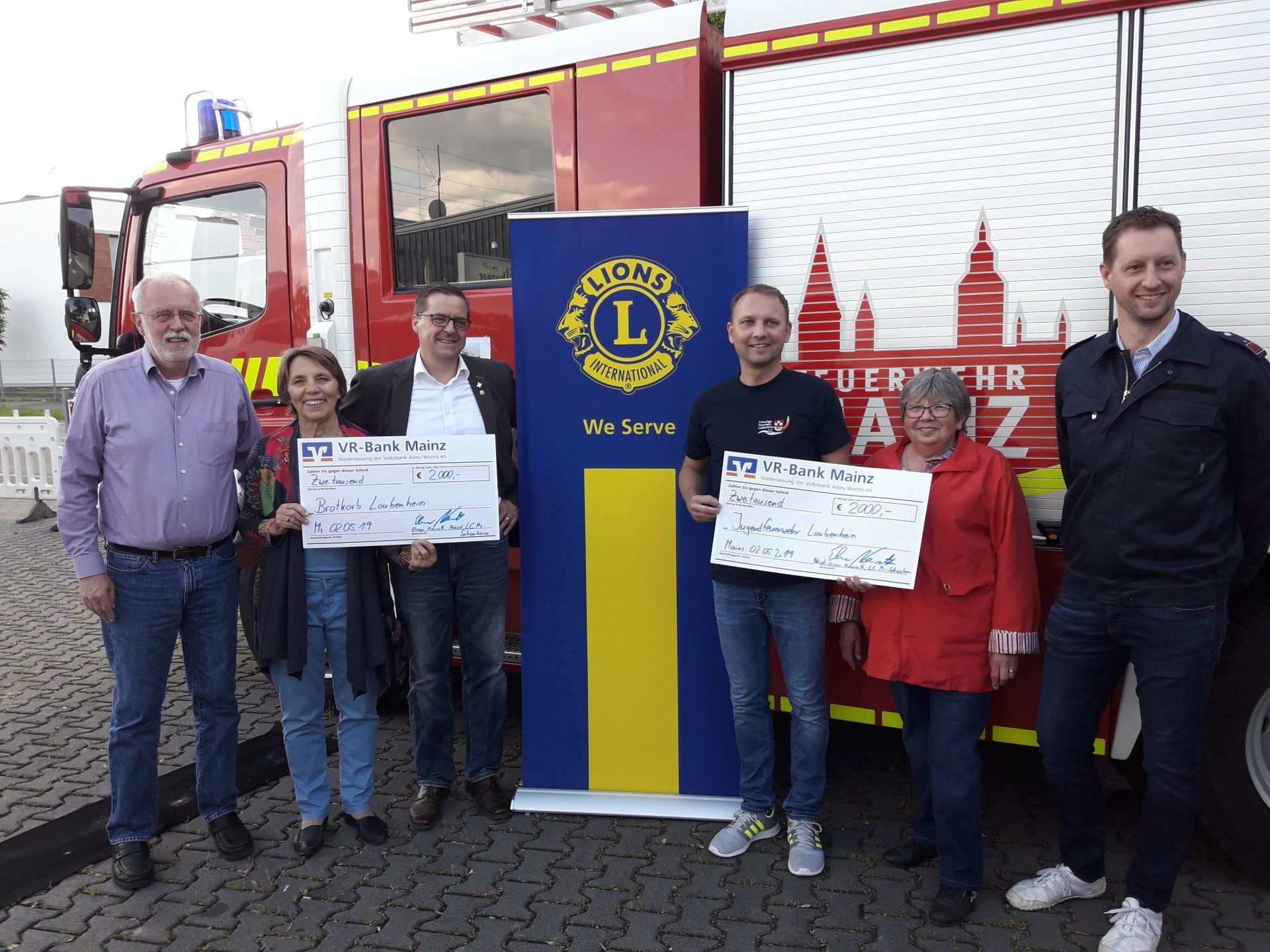 Eine Gruppe von Menschen steht mit Schecks in der Hand vor einem Feuerwehrauto.