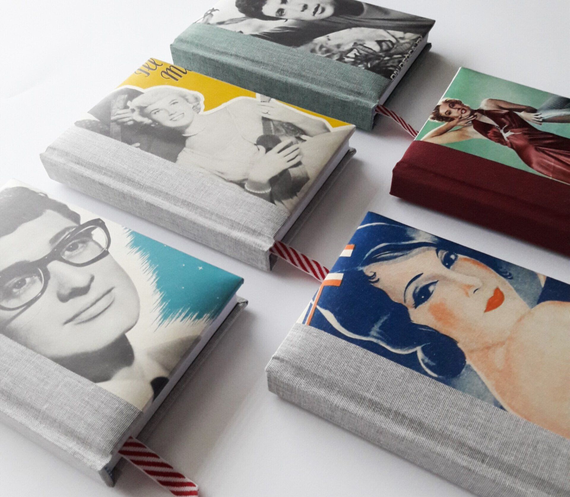 The image shows 5 pocket sized diaries with various vintage images on the cover. There is one with a black and white paper image of Buddy Holly against a light blue background and another paper colour magazine image of Marilyn Monroe in a silk red gown. There is also a black and white image of Doris Day against a yellow background and a black and white image of Tom Jones. The fifth book is a colour portrait illustration of a lady from the 1940's. The covers have a contrasting coloured cloth spine in either light grey turquoise or dark red which overlaps the paper image slightly on each diary and adds strength to the spine of the hardback diaries. The covers are padded and have various fun patterned ribbon page markers. One ribbon is in a candy cane stripy red and white style. They are laid on a white background.