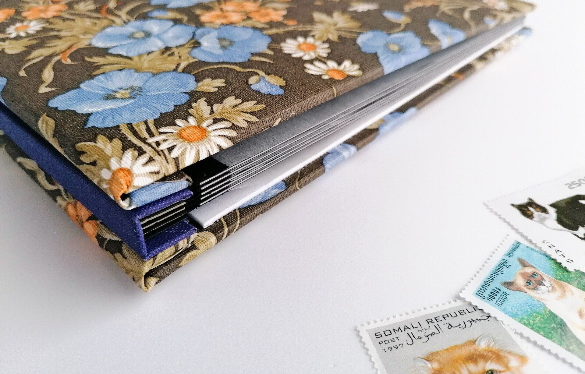 The image shows a close up of how the album is constructed and bound together using golden coloured brass screw posts. The spine of the stamp album is covered in purple cloth.