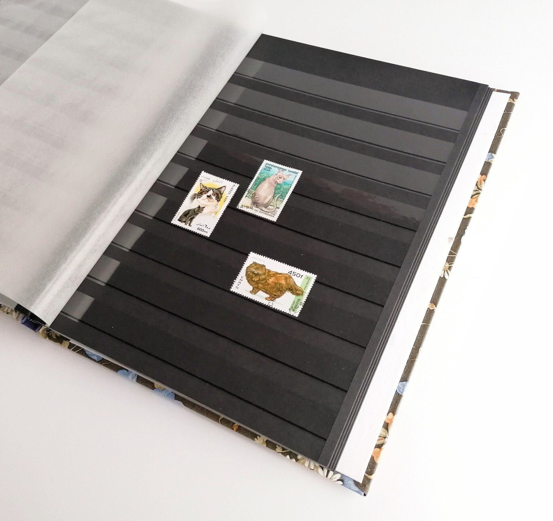 The image shows the tissue interleave turned to reveal the black page where 3 stamps with images of cats have been added to the sleeves on the pages to hold them in place.