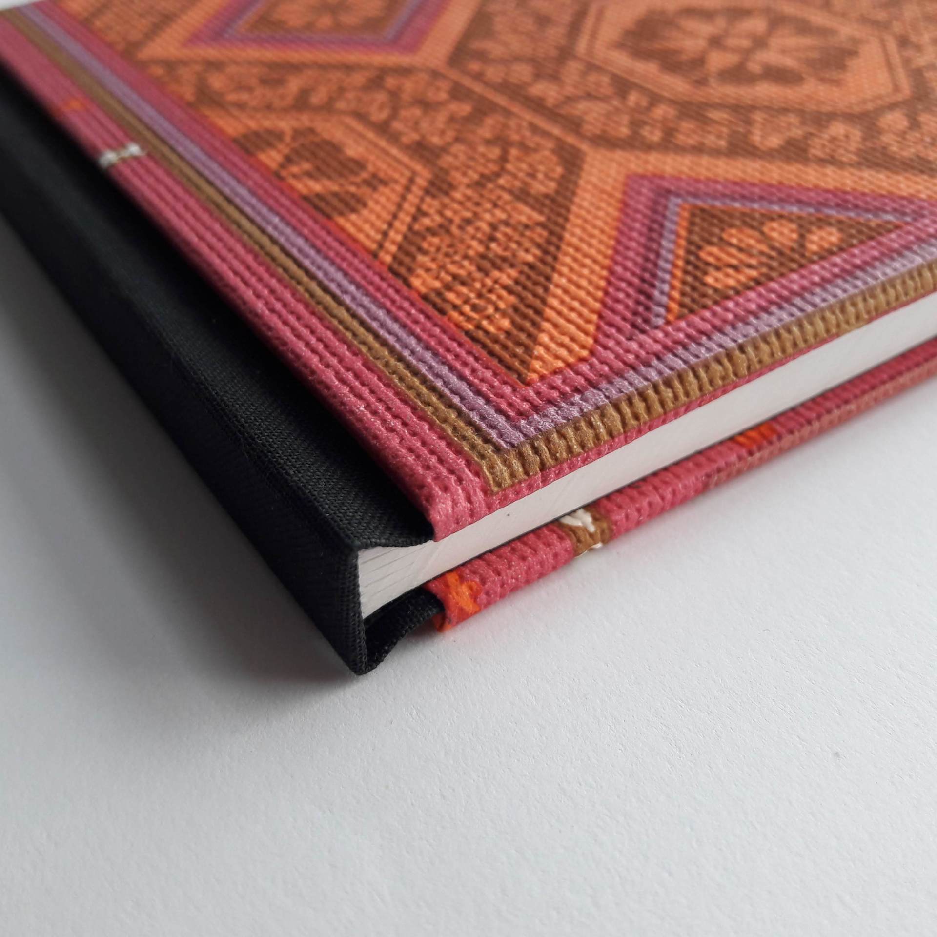 An image of a vintage upcycled wallpaper covered book. It is covered in a pink and orange retro pattern from the 1960s and 1970s. It is laid on a white background.