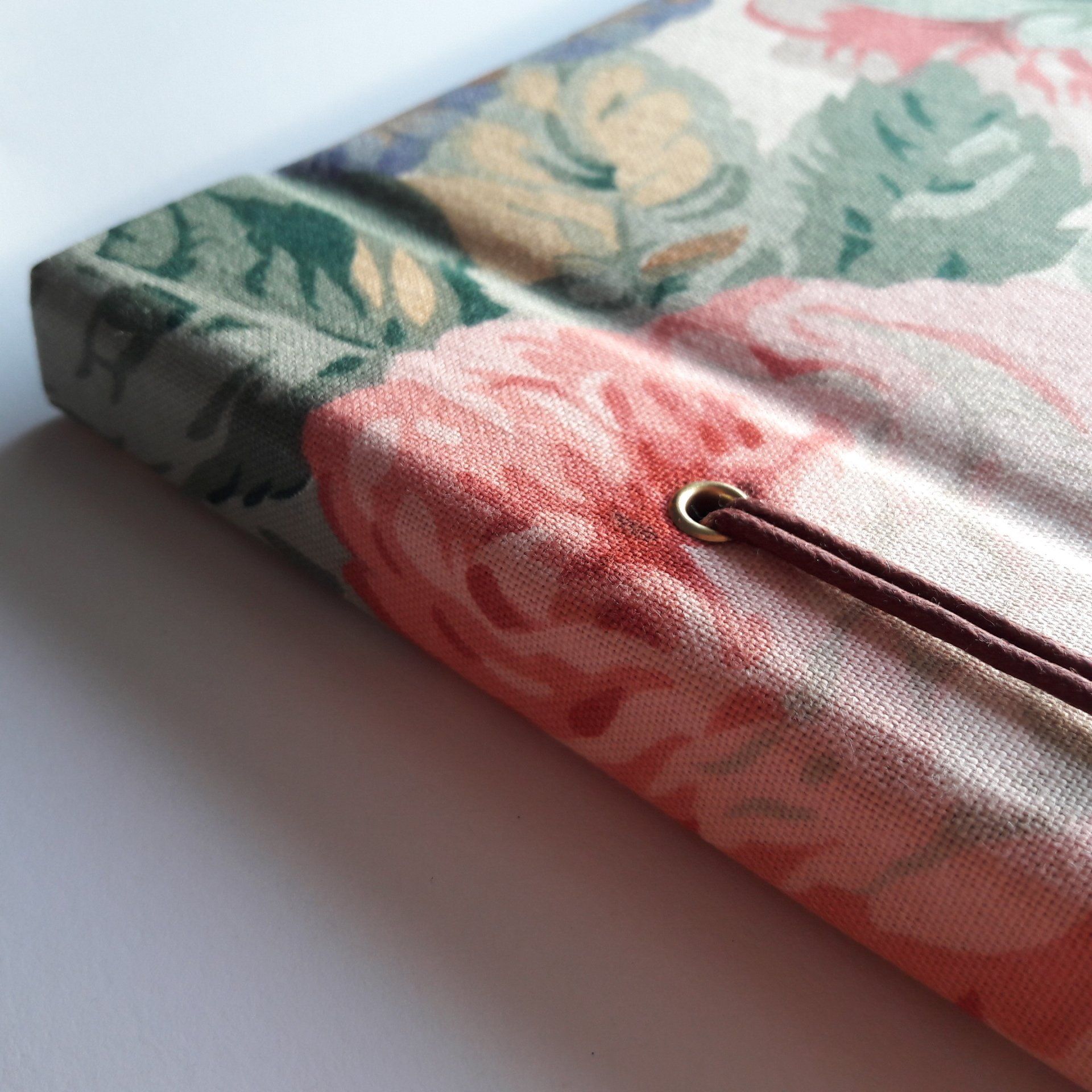 The image shows a vintage floral fabric photo album. The floral pattern on the album is in red light pink dark pink light green dark green and mustard. The album has a gold metal eyelet with dark red leather cord running through it.