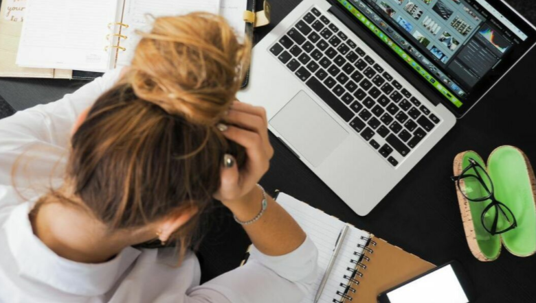 A woman is sitting at a desk with her head in her hands in front of a laptop computer.