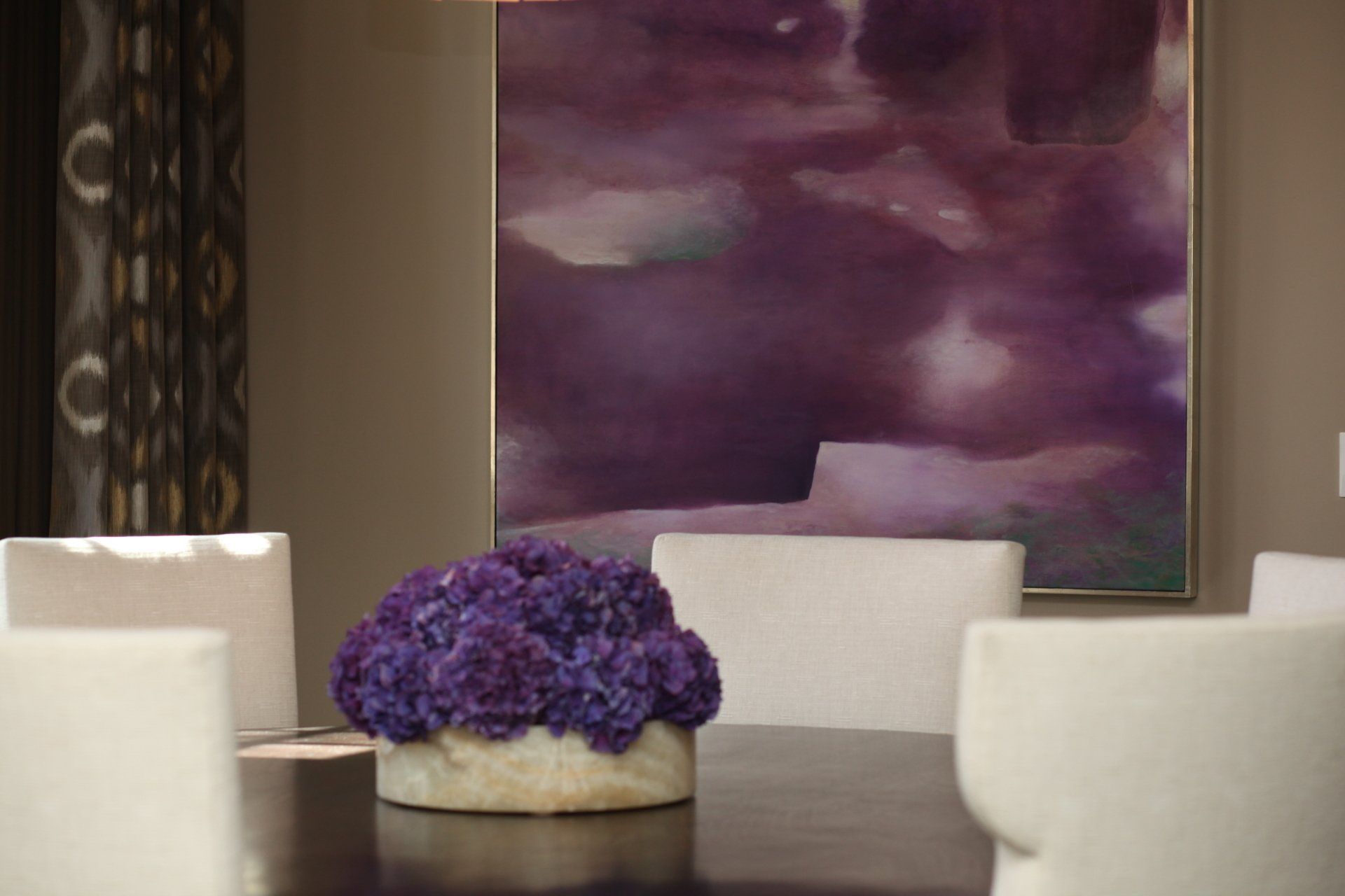 There is a vase of purple flowers on the table in the dining room.