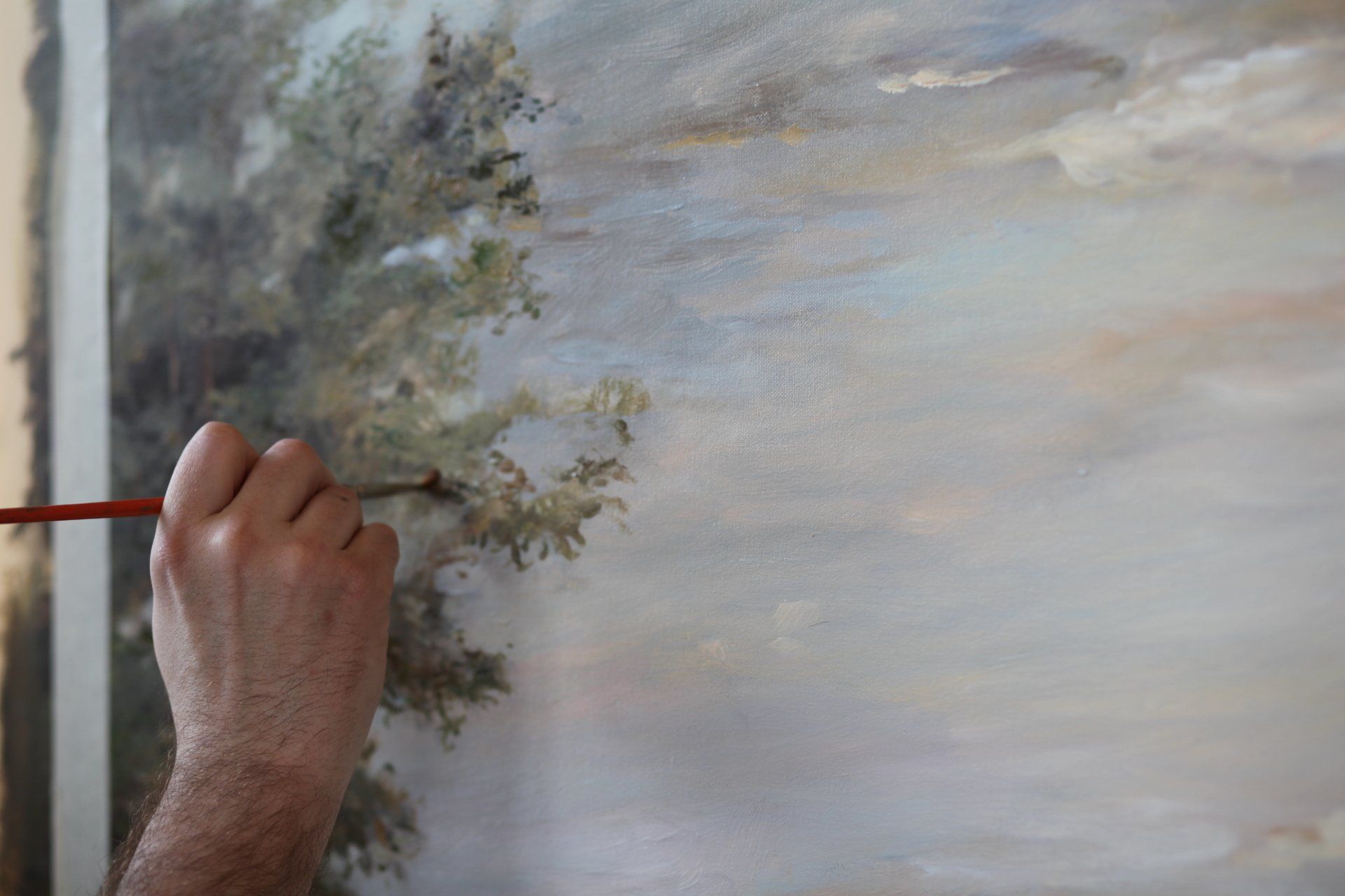 A man is painting a landscape with a brush on a canvas.
