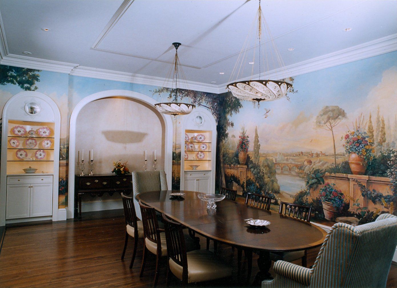 A dining room with a long table and chairs and a mural on the wall
