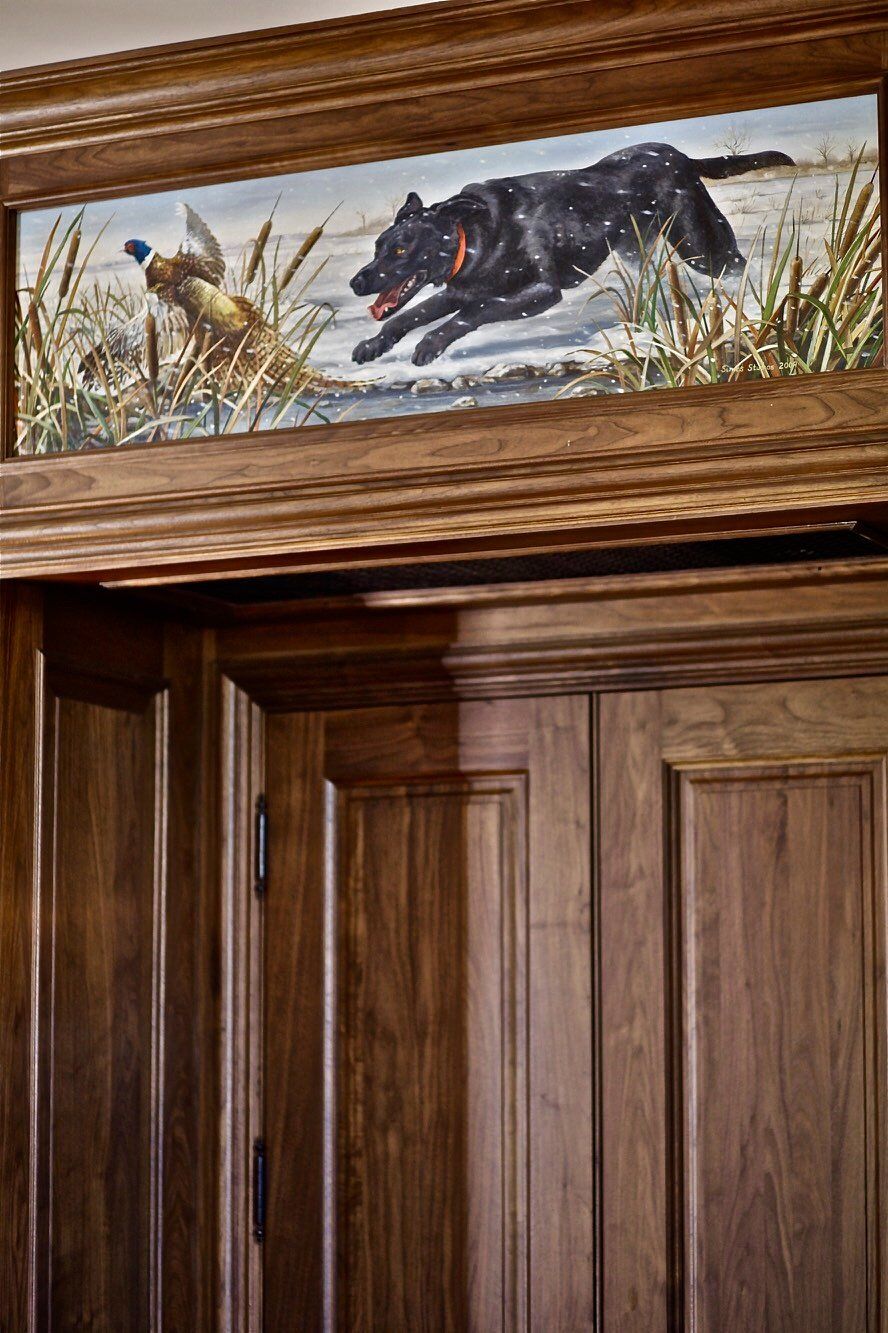 A painting of a dog chasing a pheasant is above a wooden door.
