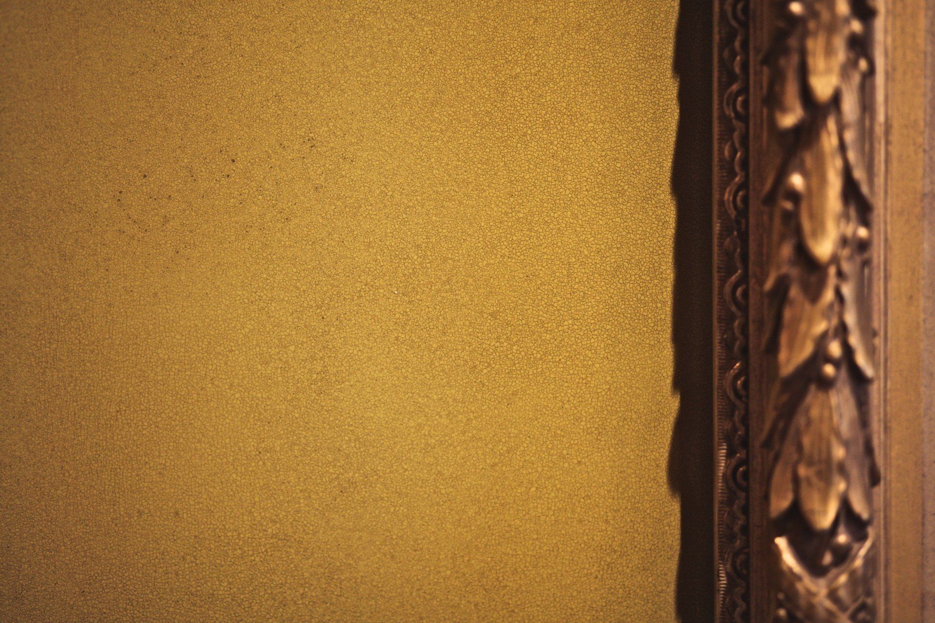 A picture frame is hanging on a wall next to a gold wall.