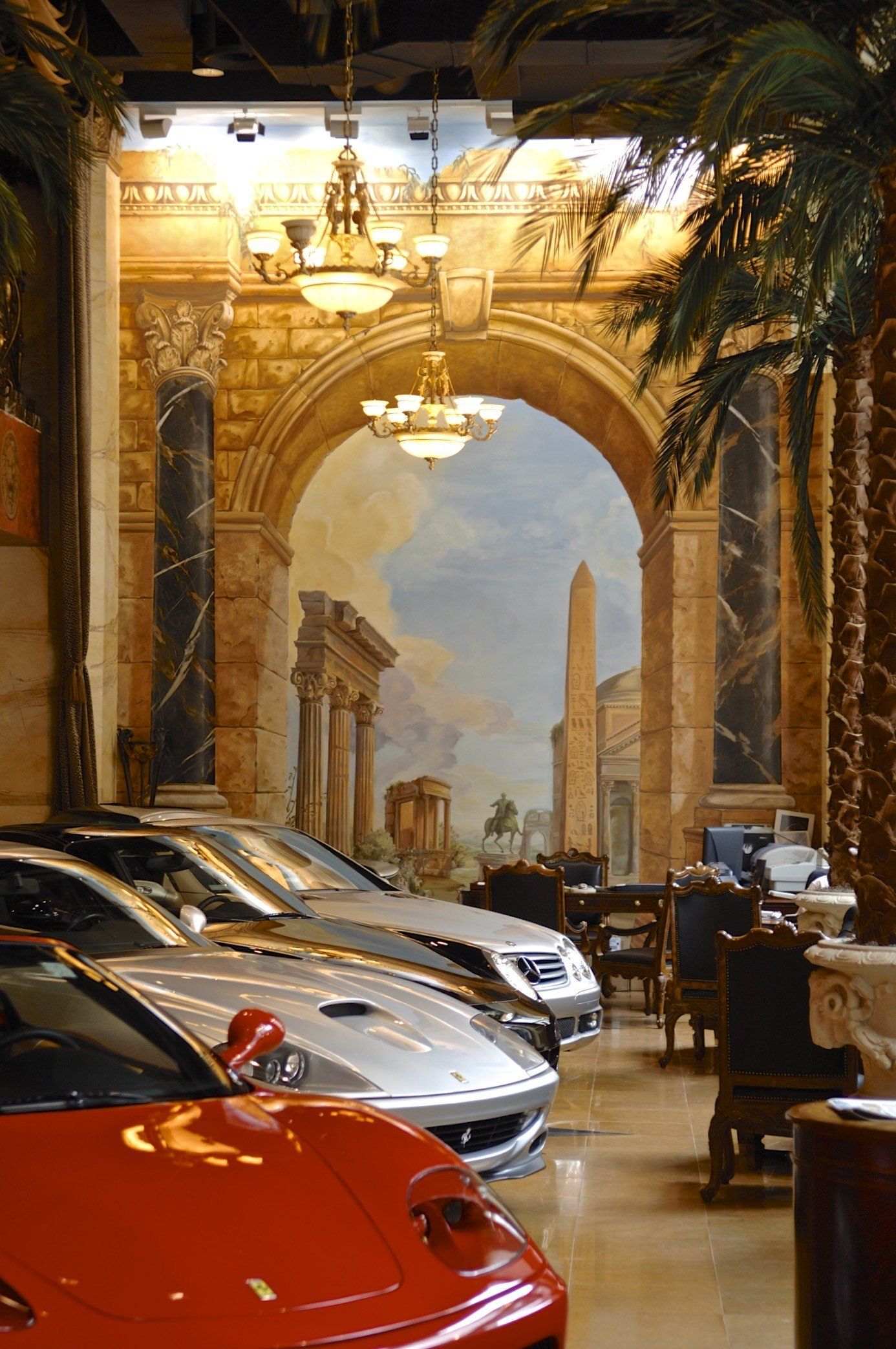 A row of cars are parked in front of a painting on the wall.