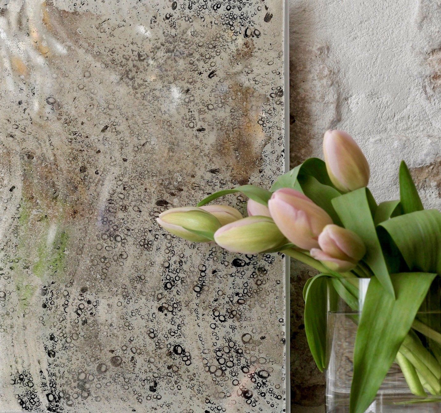 A vase of pink flowers sits next to a mirror