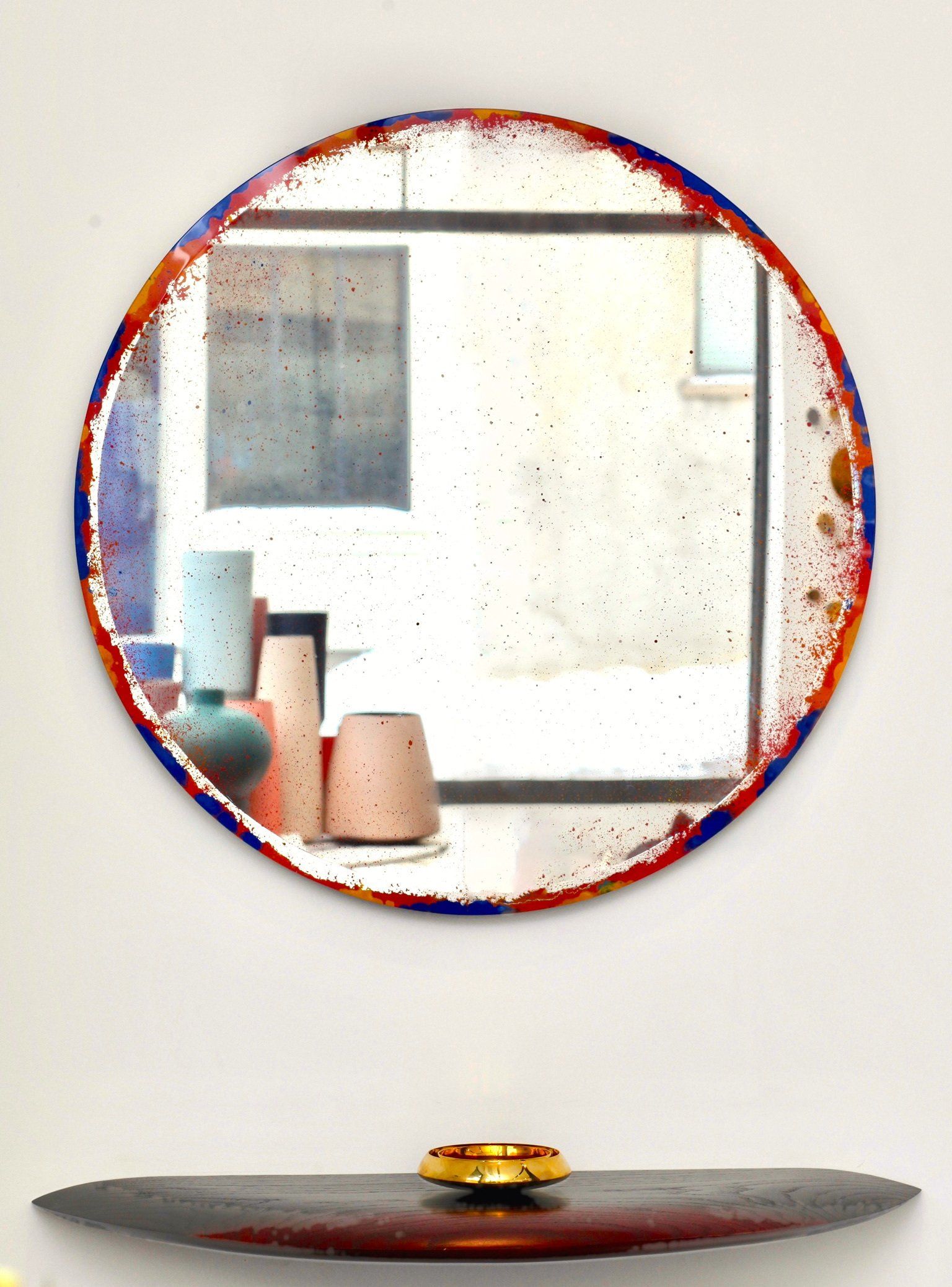 A round mirror with a colorful frame is hanging on a wall