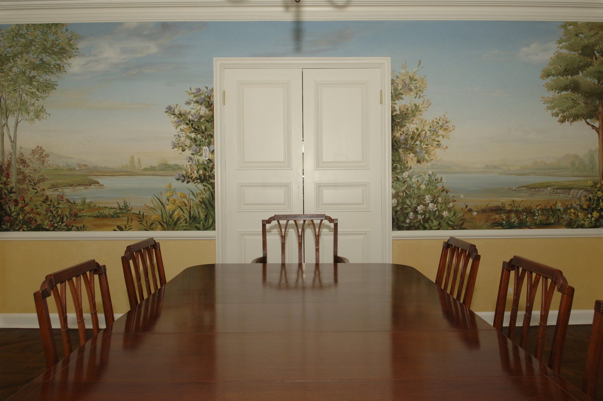 A dining room with a table and chairs and a painting on the wall