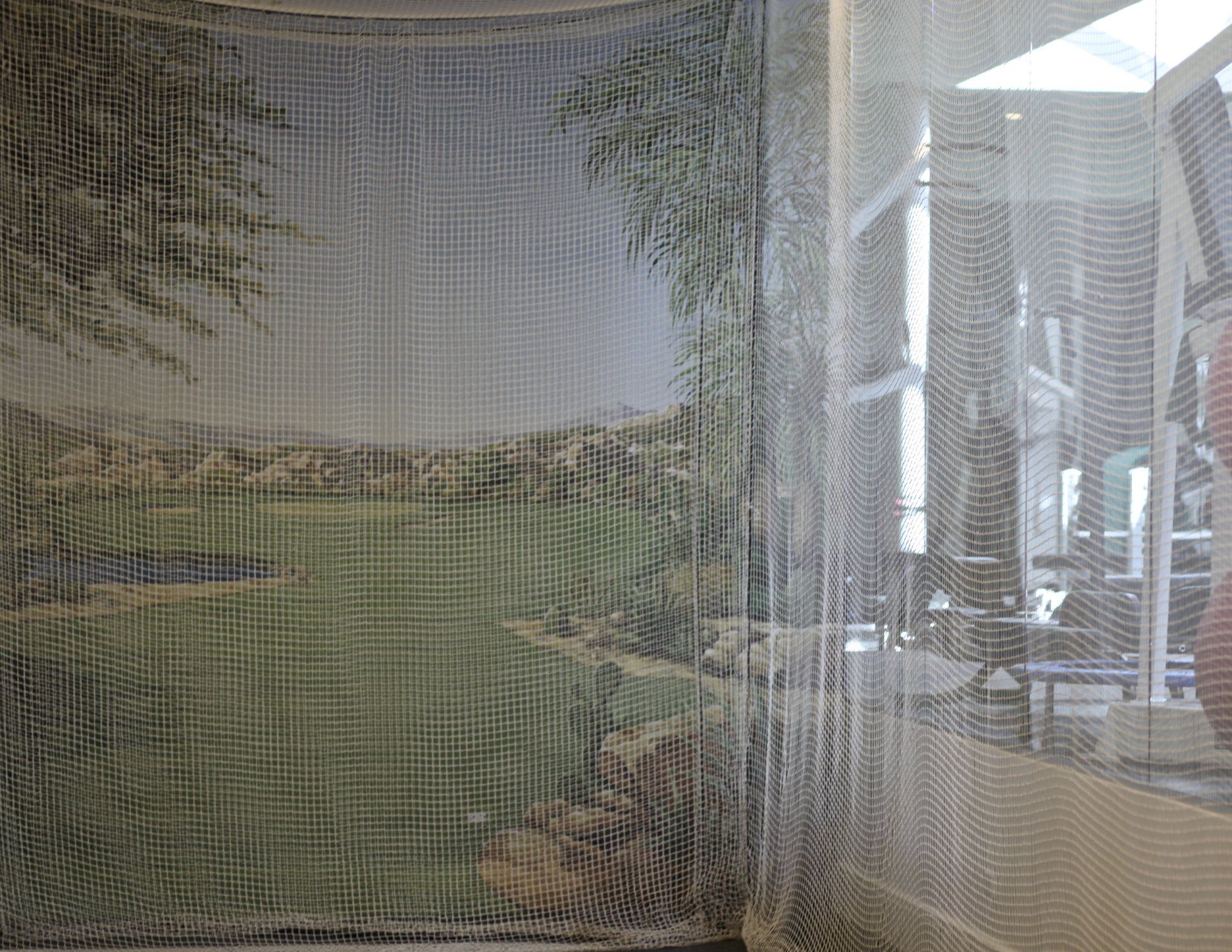 A picture of a field is behind a sheer curtain in a room.