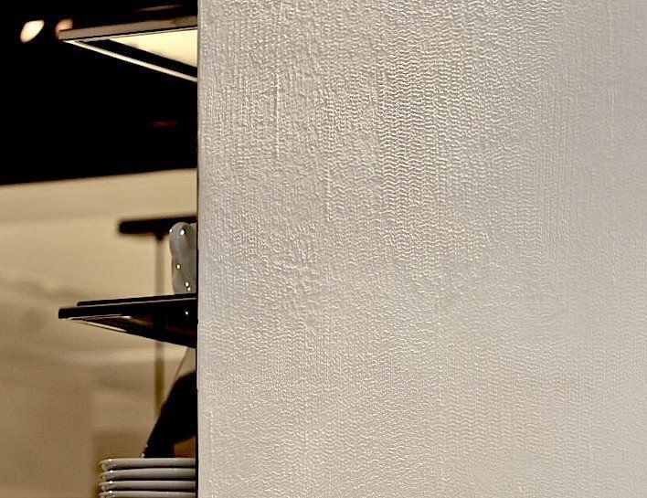 A white wall with a shelf in the background and plates on it.