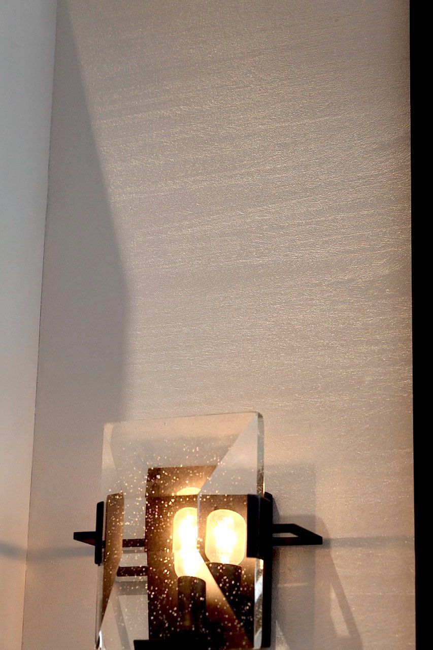 A wall light with a glass shade is hanging on a white wall.