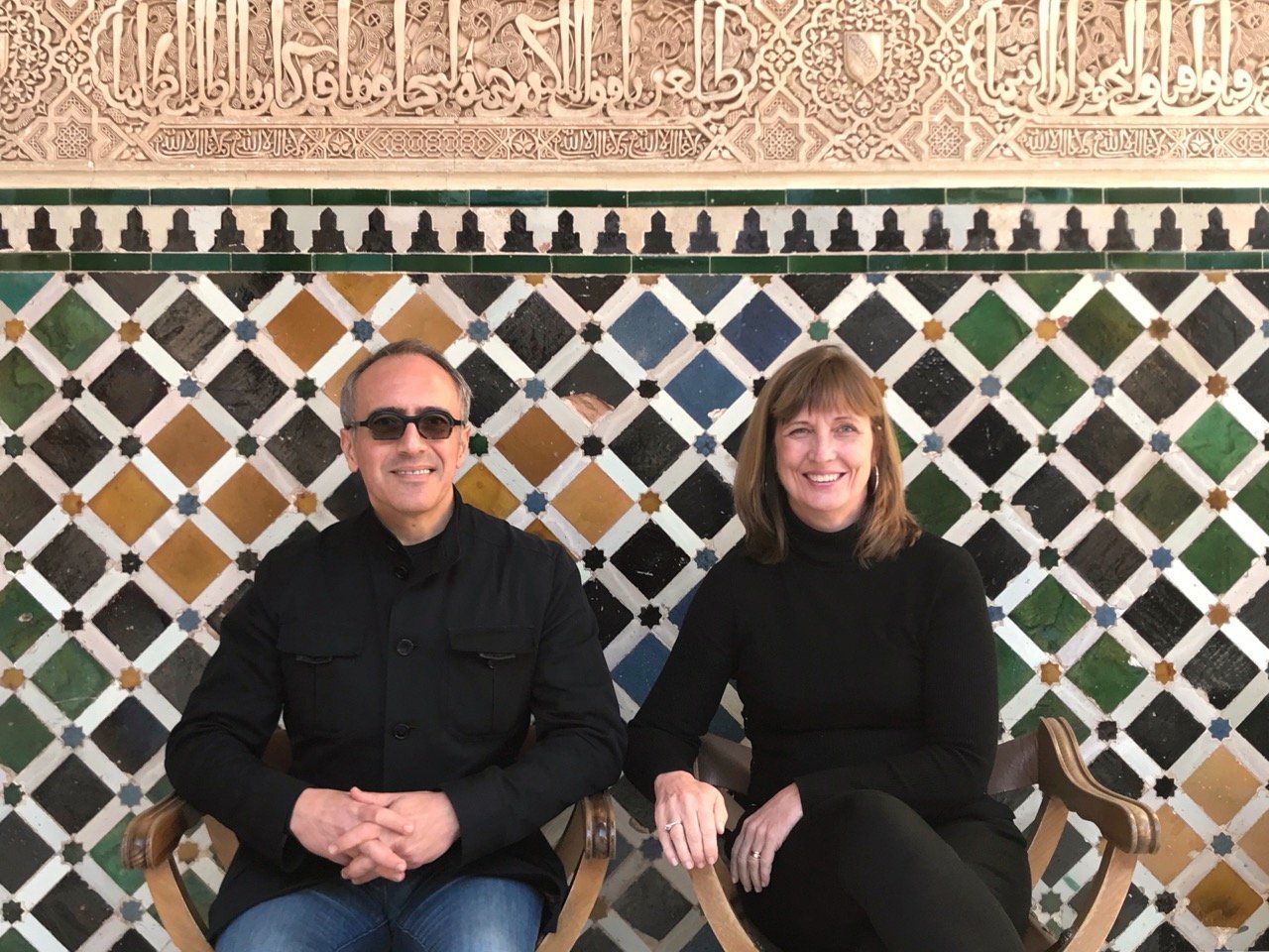 A man and a woman are sitting in front of a tiled wall.
